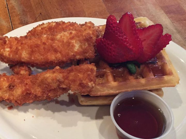 A white plate topped with fried chicken and a waffle with strawberries and syrup.