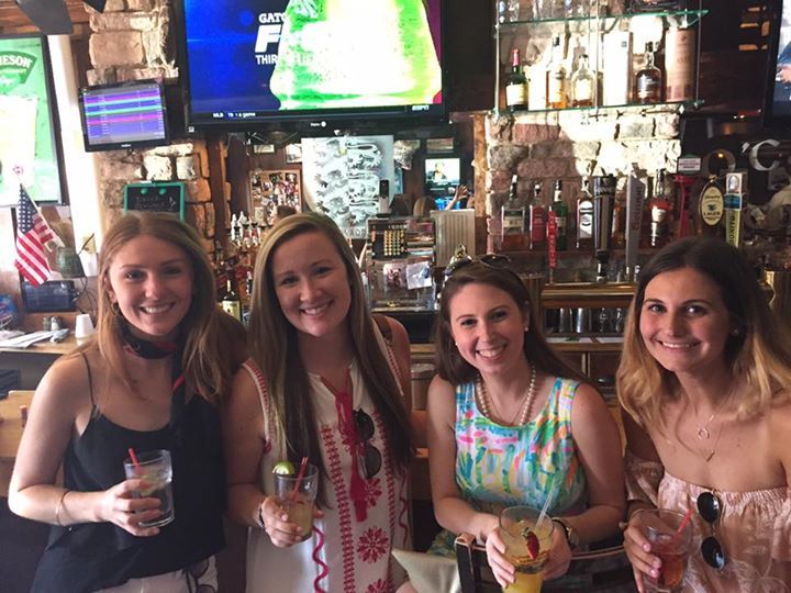 Four women are posing for a picture in a bar while holding drinks.