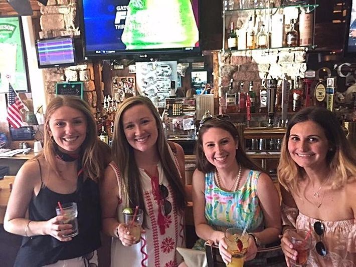 Four women are posing for a picture in a bar while holding drinks.