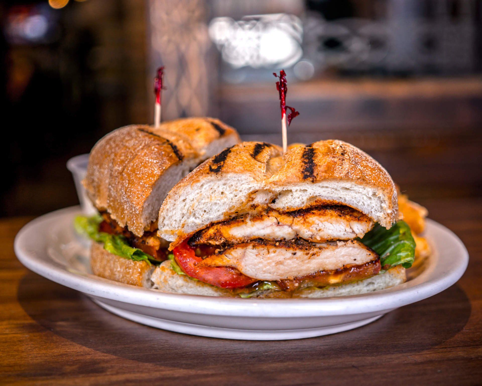 A grilled chicken sandwich on a white plate on a wooden table.