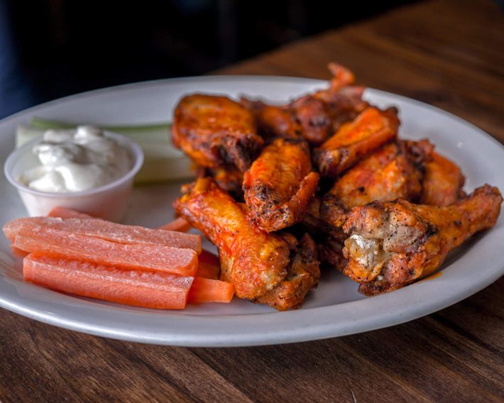 A white plate topped with chicken wings and carrots on a wooden table.