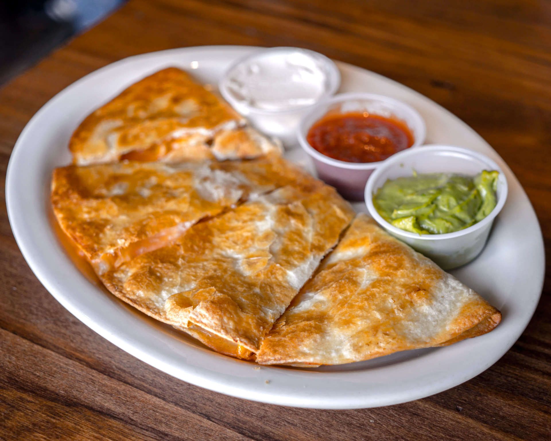 A white plate topped with quesadillas and sauces on a wooden table.