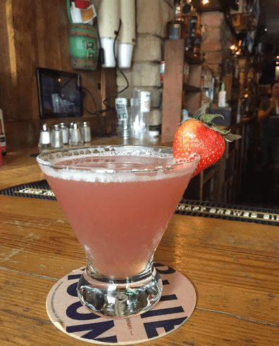 A martini with a strawberry on top of it is on a wooden bar.