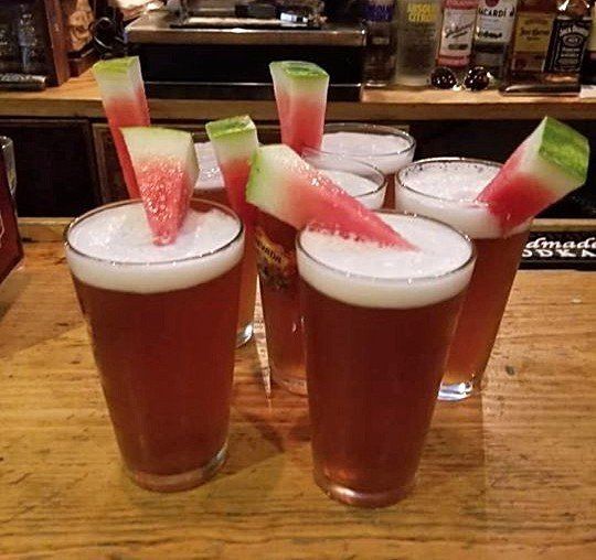 Four glasses of beer with watermelon slices in them