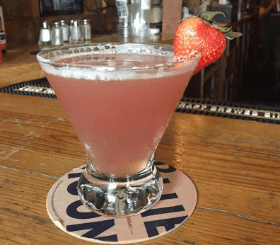 A martini with a strawberry on top is on a wooden bar.