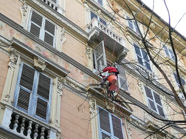 tre persone con delle imbracature al lavoro sulla facciata di un palazzo
