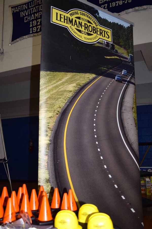 Banner for Lehman-Roberts featuring a winding road. Orange cones and yellow helmets in foreground.