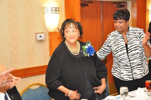 Woman in black dress with jewelry, and a woman in zebra print top, in a banquet hall.