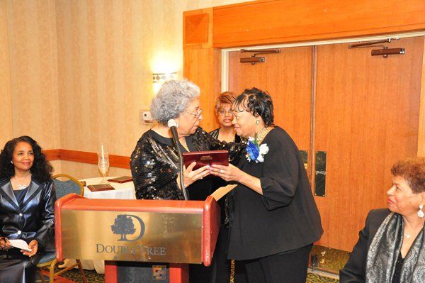 Woman receiving a gift at a podium in a banquet hall. Others observe.