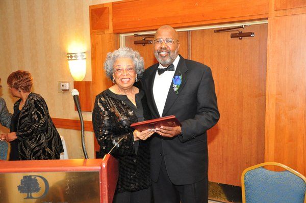 Man in a suit presents an award to a woman in a sparkly dress at an event.