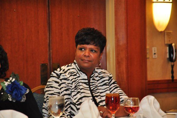 Woman in zebra-print jacket sits at a table with drinks and napkins, looking to the side. Wooden paneling in background.