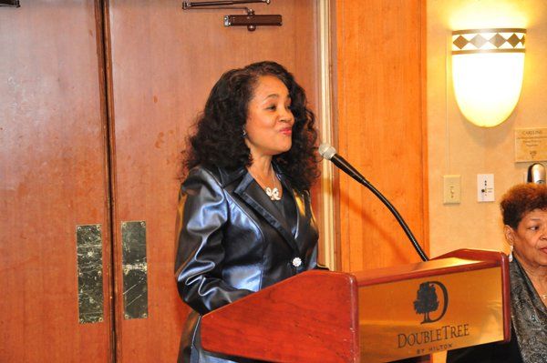Woman at podium with microphone, speaking. DoubleTree hotel logo on the podium.