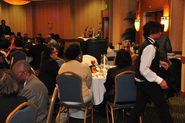 People seated at tables in a banquet hall. A server in a black vest walks by, carrying a tray.