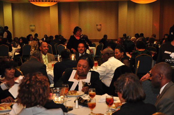 People seated at tables in a brightly lit banquet hall. They are eating and socializing.
