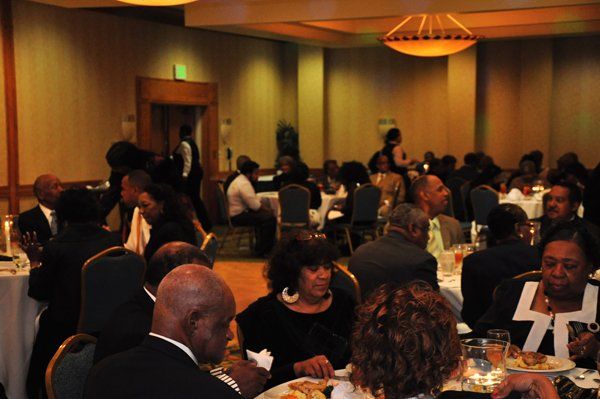 People seated at tables in a banquet hall, possibly a dinner event; many are wearing black attire.