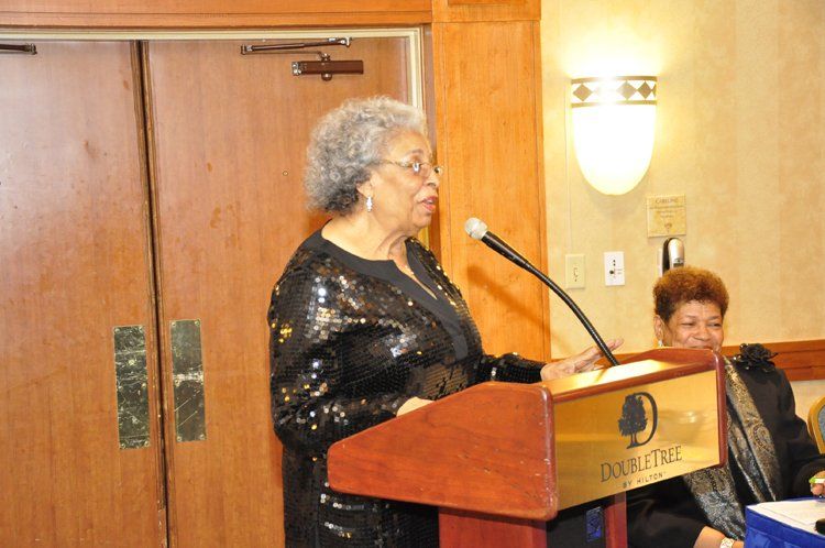 Woman speaking at a podium with a microphone, in a room with a hotel logo.