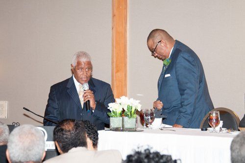 Man speaking into microphone, another man beside him, possibly an event or conference.