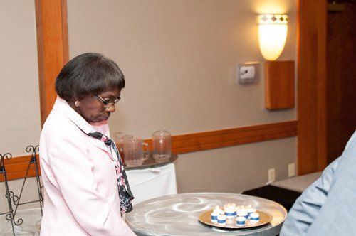 Woman in pink jacket examines items on a small table in a room with neutral walls.