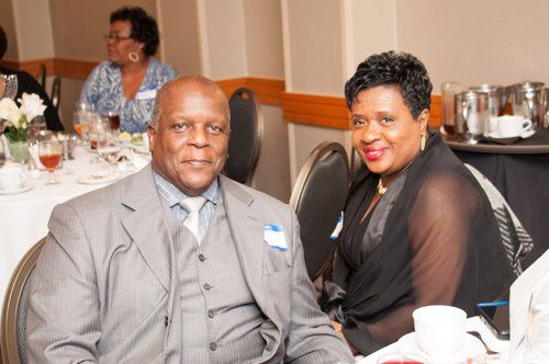 Man and woman at a table; man in gray suit, woman in black; smiles at an event.