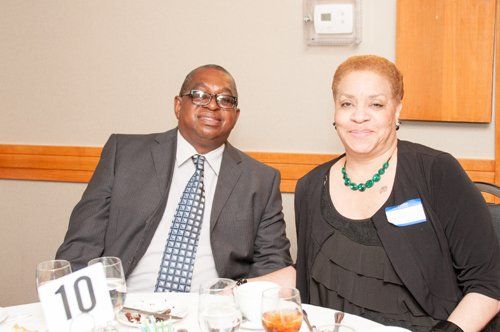 Two people seated at a table. Man in suit and tie. Woman in black top and necklace. Both smiling. Number 10 on the table.