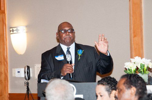 Man in a suit speaking at a podium, gesturing with his hand.
