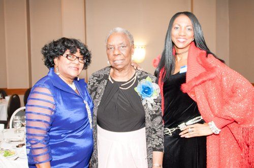 Three women posing together at a formal event, one in blue, one in black, and one in red.