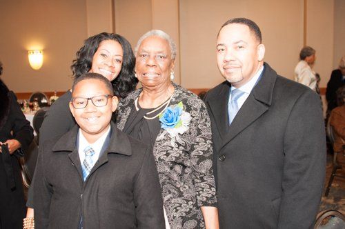 Family poses together indoors: woman with a flower, three others smiling in formal attire.