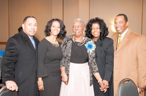 Five people posing for a photo. A woman in a floral pin is flanked by two women and two men, all dressed formally.