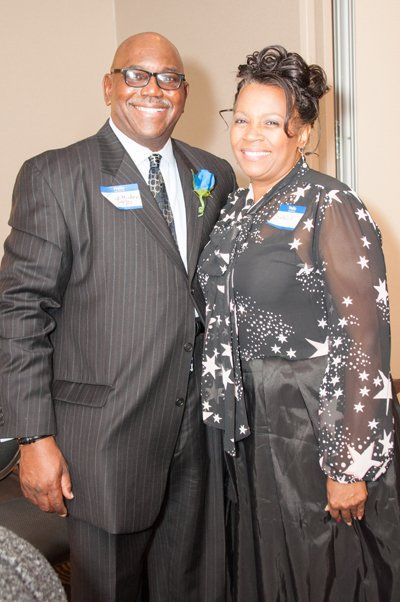 Man in pinstripe suit and woman in star print blouse, smiling, posing together at an event.
