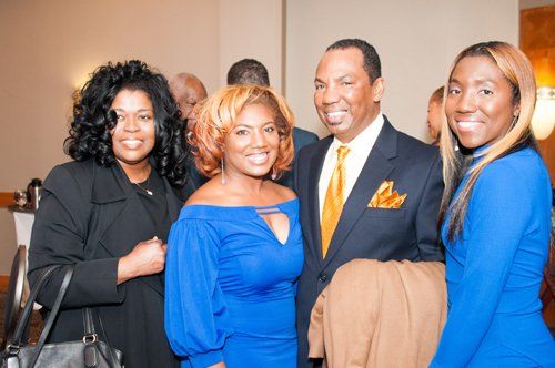 Four formally dressed people smiling together indoors.