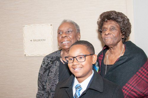 Young person in glasses with two older adults, smiling, by a 