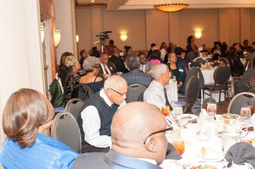 People seated at tables in a banquet hall, attending an event. Tables are set, and guests are conversing.