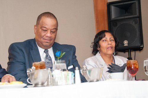 Man and woman at a table; man in blue suit, woman in light jacket, near a speaker.