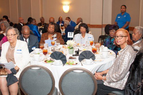 People seated around tables at an event; food, flowers, and decorations are present.