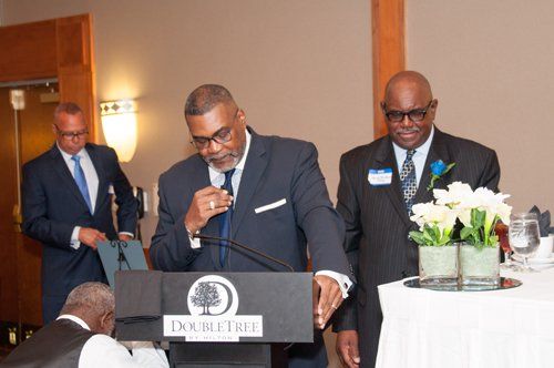 Men at a podium, one speaking into a microphone at a DoubleTree event.