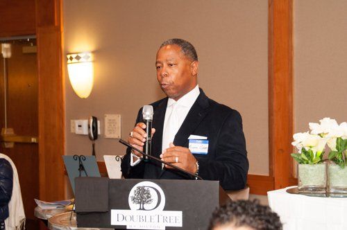 Man speaking at a podium with a microphone at a DoubleTree event.