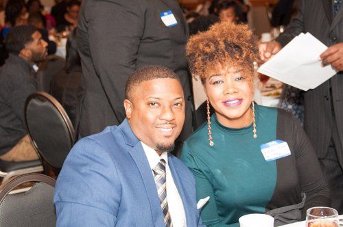Man in blue suit and woman in teal top smile at the camera, seated at a table.