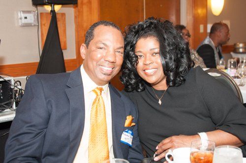 Man and woman smiling at a table, man in a suit with gold tie, woman in black dress.