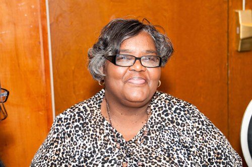 Woman with glasses and a leopard print shirt smiles, seated in a wood-paneled room.