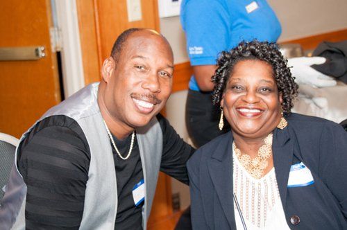 Two smiling people, a man with a shaved head and a woman with curly hair, pose close together.