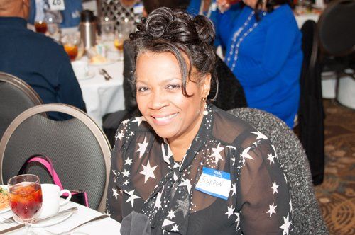 Woman smiling at a table, wearing a star-patterned shirt, at an event.