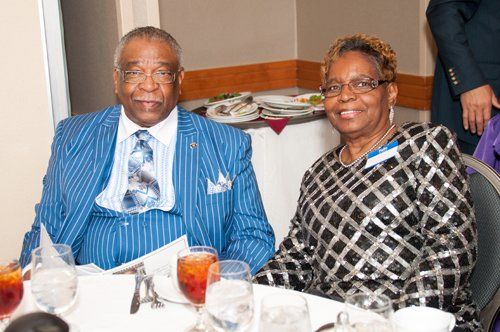 Couple seated at a table, man in blue striped suit, woman in black and silver patterned top, dining.