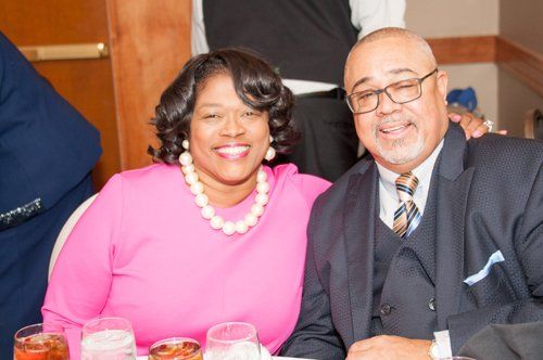 Woman in pink dress and man in suit smiling at a table, indoor setting.