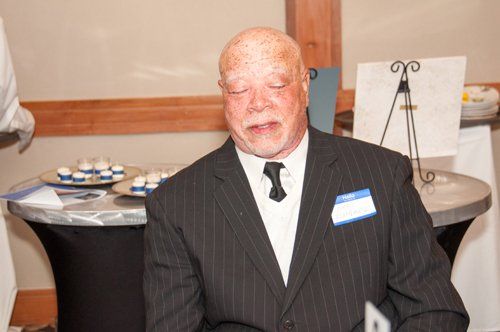 Man in pinstripe suit at an event, with light skin and freckles. He has a nametag.
