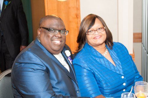 Couple smiling, in formal blue attire, seated at a table, indoors.