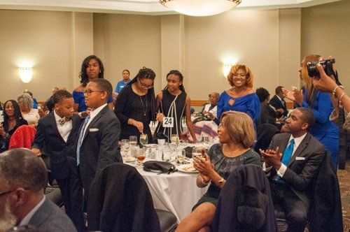 People at an event, some applauding, others at a table with food, in a room with sconces.