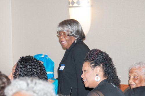 Group of people at an indoor event, woman with grey hair smiles, others laugh.