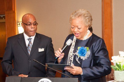 Man and woman at podium; woman speaks into microphone, reading from document; formal setting.