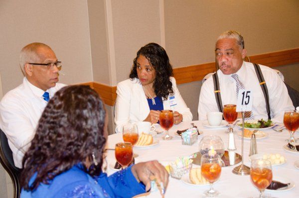 Four people seated around a table, engaged in conversation. Drinks and plates are visible; a conference setting.