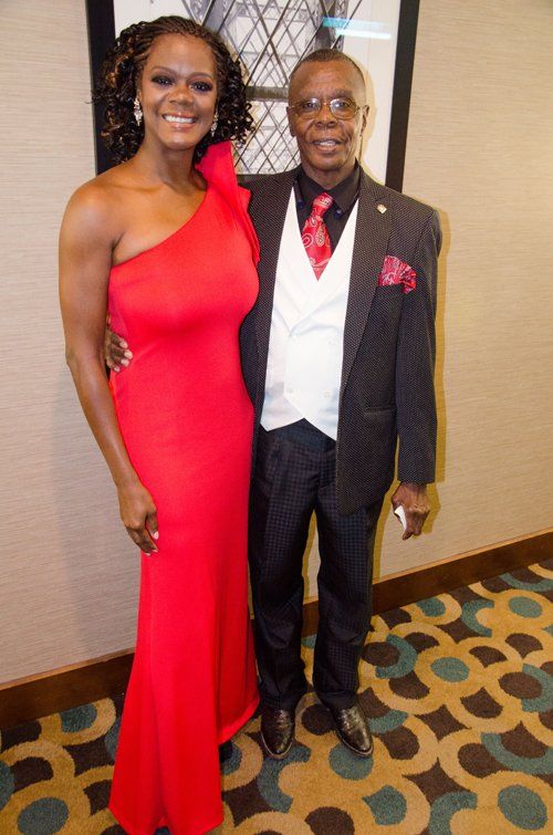 Woman in red gown and man in suit, posing indoors.
